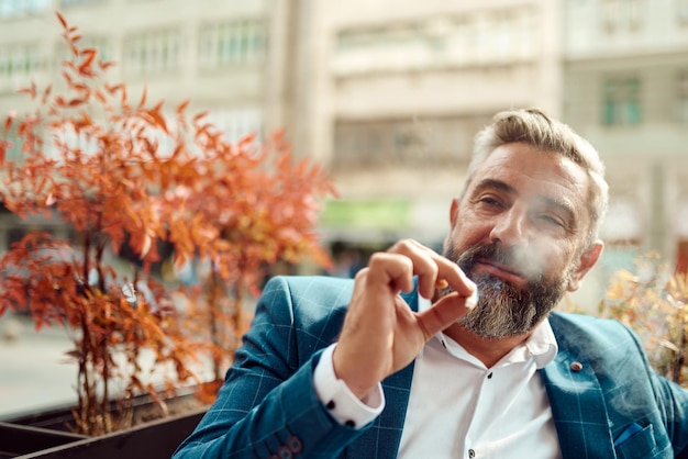 Современный старший бизнесмен курит сигарету во время отдыха в кафе после тяжелого рабочего дня.