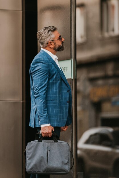 Modern senior businessman with a bag exits modern corporation.