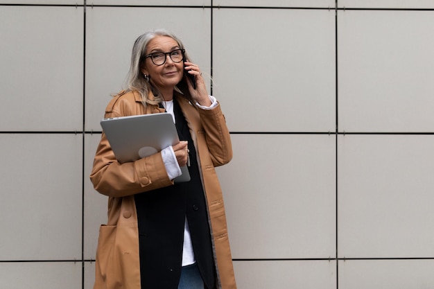 Modern senior businesswoman talking on a mobile phone with a laptop in her hands against the