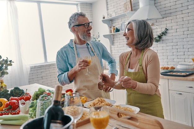 Modern senior couple in aprons preparing healthy dinner and smiling while spending time at home