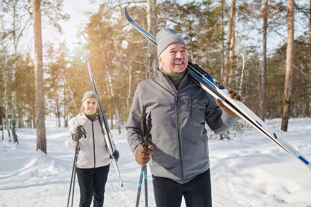 Modern senior couple carrying skis and poles