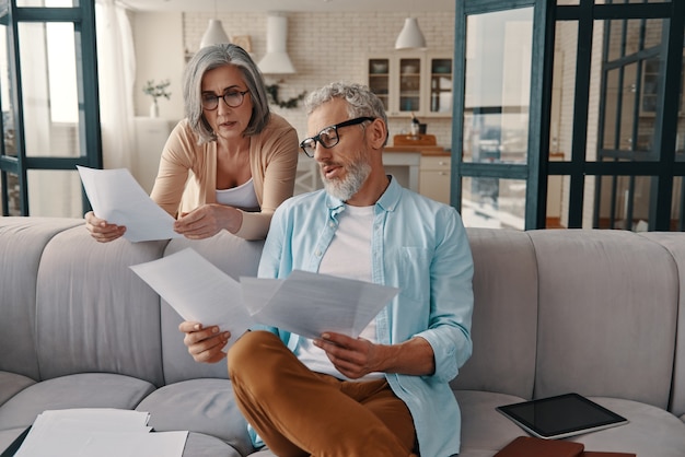 Modern senior couple in casual clothing taking care of their finances while bonding together at home