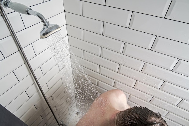 Modern shower with a watering can from which warm running water is sprayed and falls on male back