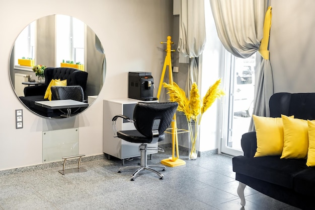 Photo modern small bright hair and beauty salon in black and yellow colors with gray walls and floor and black sofa with yellow cushions