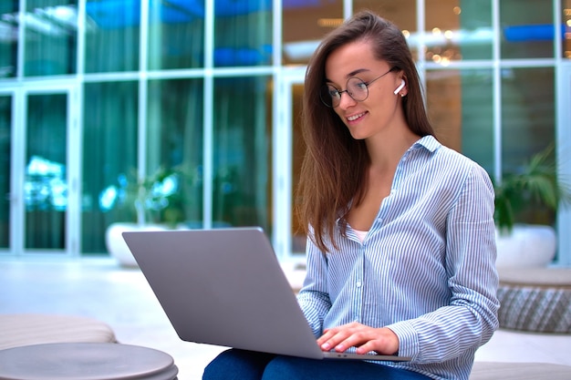 Modern smart freelancer woman wearing wireless headphones remotely working online at a computer