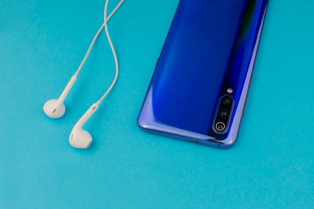 modern smartphone with musical headphones on a blue wall