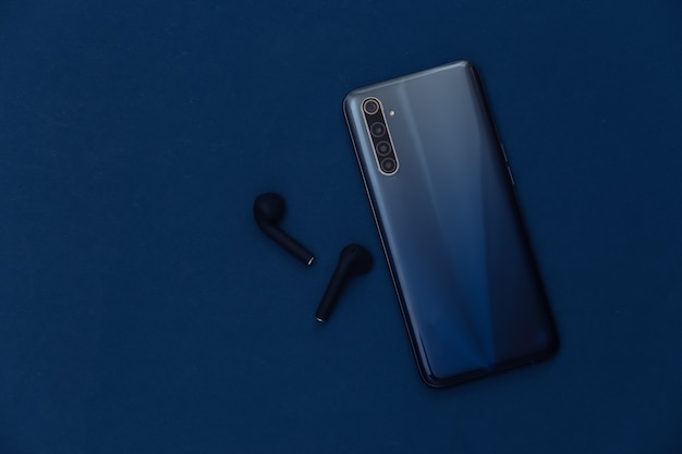 Modern smartphone with wireless earphones on classic blue background.