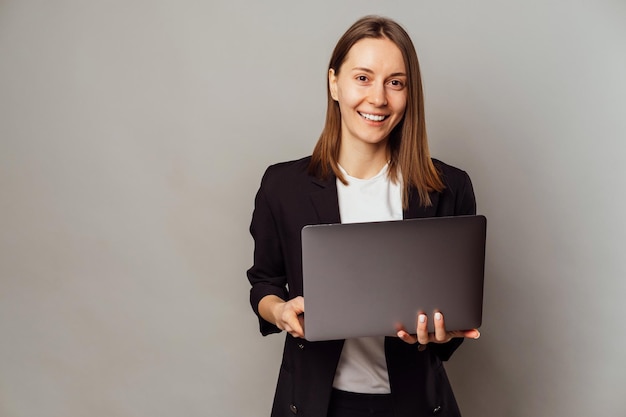 Modern smiling woman standing in a studio is holding an opened laptop