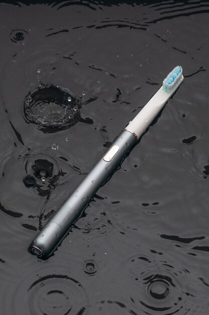 写真 モダンなソニック電動歯ブラシ グレーの金属製 プロフェッショナルな口腔ケアと健康な歯 ミニマルなデザイン 彼らは水の中に横たわっています 黒の背景