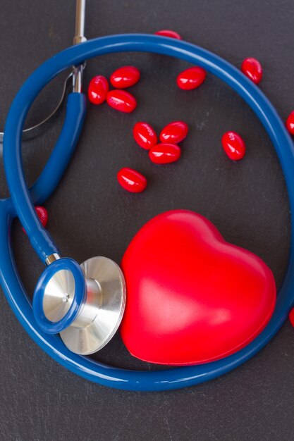 Modern stethoscope with red heart and pills on black background