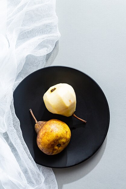 Modern still life, whole and peeled pears in a black plate on a gray table