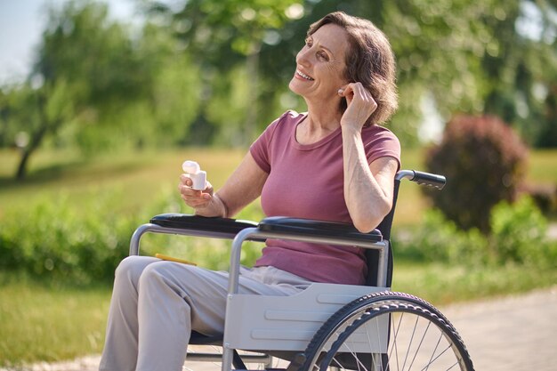 Современные вещи. Улыбающаяся женщина в инвалидной коляске надевает беспроводные наушники