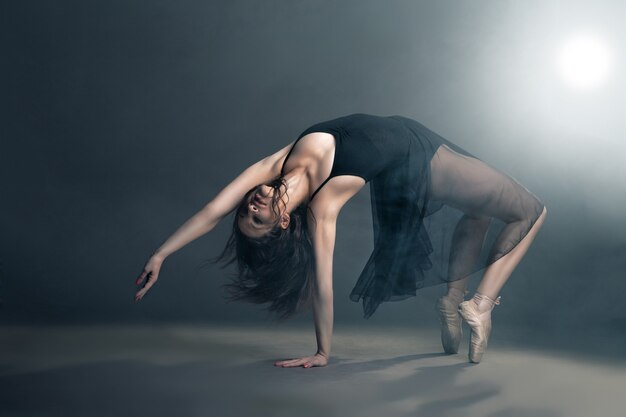 Modern style dancer posing on a studio grey background in fog