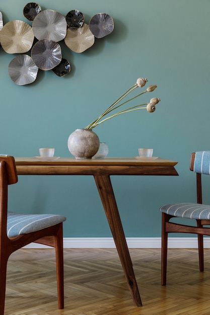 Современный и стильный интерьер столовой с гламурным деревянным столом, элегантными стульями и дизайнерским декором. Шаблон. Домашний декор. Зеленая второстепенная стена.