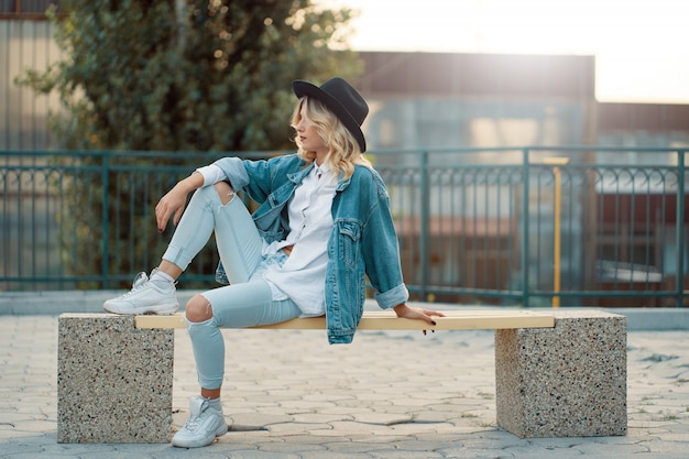 A modern, stylish girl posing while sitting on a minimal city be