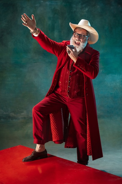 Modern stylish Santa Claus in red fashionable suit and cowboy's hat on dark background