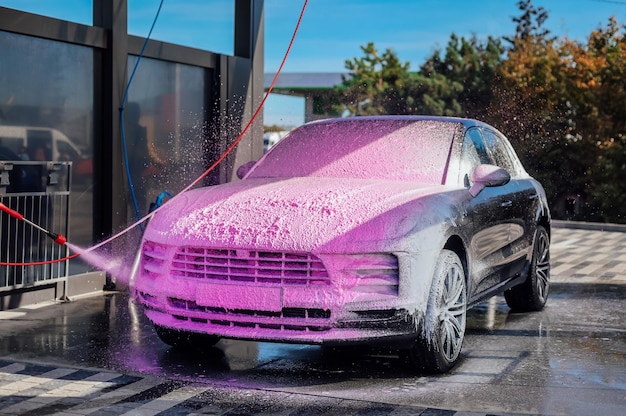 Modern suv car covered with pink soap foam in self wash station