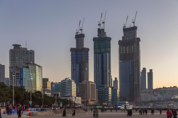 Modern tall houses on the embankment of the sea coast in the evening setting sun People walk on a large sandy beach Busan South Korea 20180101