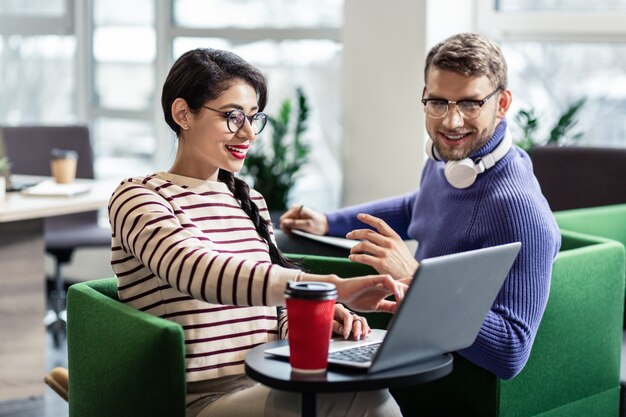 Modern technologies. Delighted bearded man keeping smile on his face while looking at computer