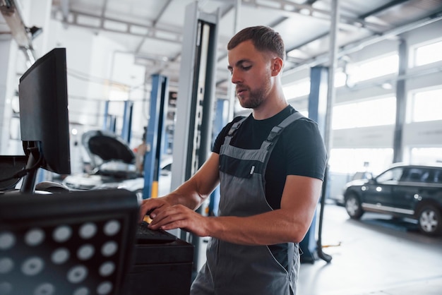 modern technologies man at the workshop in uniform use computer for his job for fixing broken car