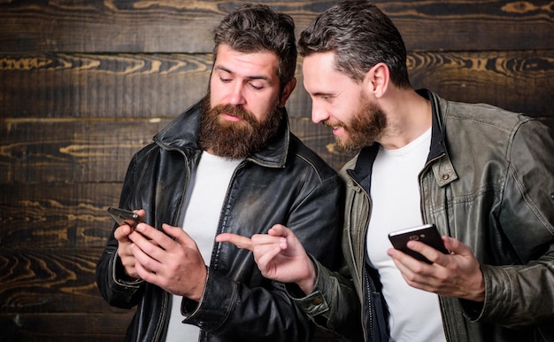 Modern technology Men with smartphones surfing internet Mobile internet Business application Men brutal bearded hipster in fashionable leather jackets use mobile internet Online business