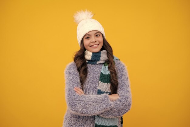 Modern teen girl wearing sweater and knitted hat on isolated yellow background happy girl face positive and smiling emotions