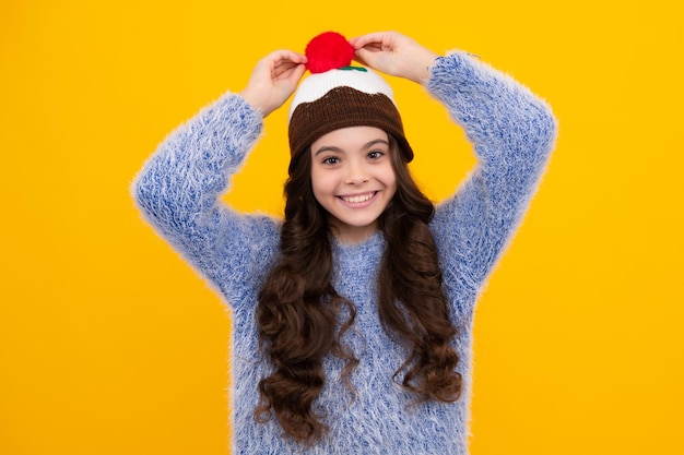 Modern teen girl wearing sweater and knitted hat on isolated yellow background happy teenager positive and smiling emotions of teen girl