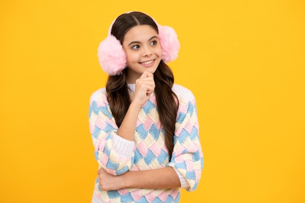 Modern teenage girl 12 13 14 year old wearing sweater and winter warm earmuff earflaps hat on isolated yellow background