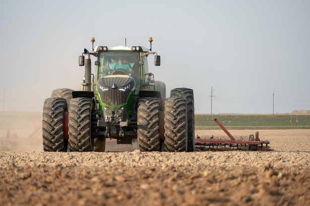 A modern tractor with a trailed plow works in the field Plowing the land before sowing grain crops Young farmer tractor driver of agricultural production
