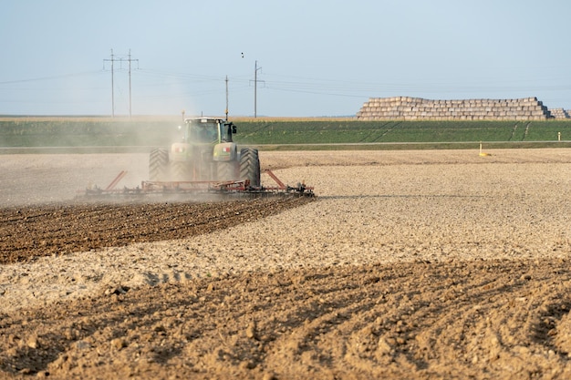 A modern tractor with a trailed plow works in the field Plowing the land before sowing grain crops Young farmer tractor driver of agricultural production