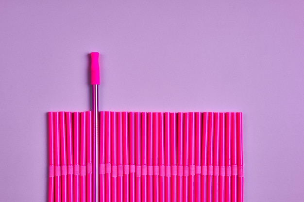 The modern trend towards caring for the environment. Reusable metal beverage straw amongst a pack of pink plastic beverage straws.