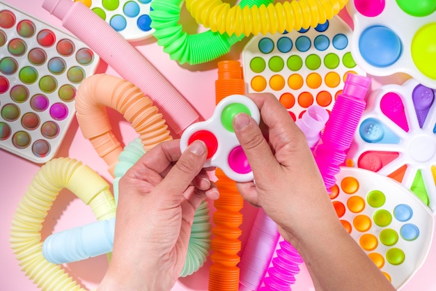 Современные модные детские игрушки для пальцев, концепция релаксации - женские руки играют с разными яркими всплывающими элементами, простыми ямочками, мягкими, поп-трубками, на белом фоне, копией пространства сверху