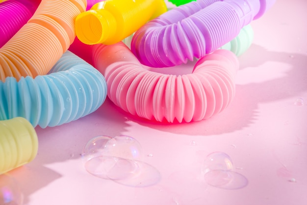 Современные модные детские игрушки для пальцев, концепция релаксации - набор различных ярких pop-it, simple-dimple, squishy, pop-tube, на красочном розовом фоне, пространство для копирования сверху