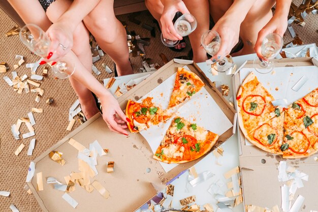 Modern trendy meisjesfeest. Jonge dames die uit het eten van pizza hangen, champagne drinken. Confetti rondom, dekvloer.