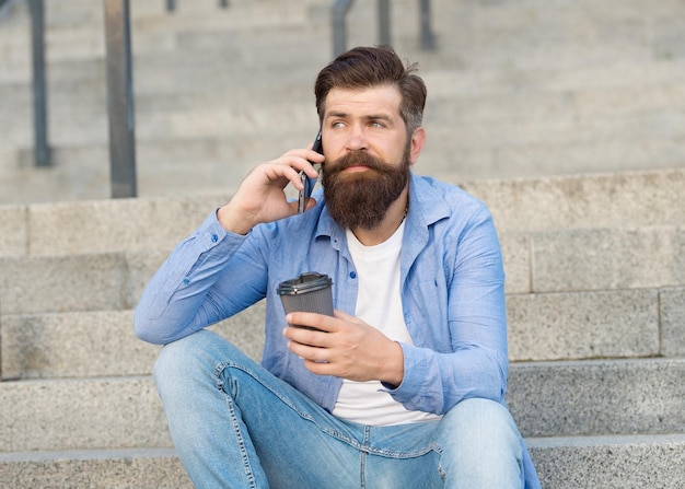 Modern urban life. Bearded man phone conversation. Mobile conversation. Coffee break. Personal communication. Calling friend. Pleasant conversation. Real connect. Drink coffee while talking.