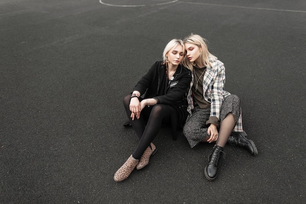 Modern urban twin sisters in beautiful casual wear sits on playground in city