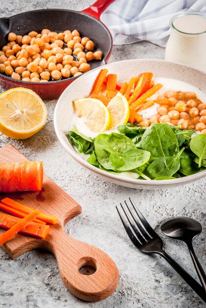 Modern veganistisch eten, hartige yoghurtkom met bonen, kikkererwten, spinazie, pittige wortelen, citroen, grijze stenen oppervlak, kopie ruimte