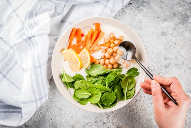 Modern veganistisch eten, persoon eet hartige yoghurtkom met bonen, kikkererwten, spinazie, pittige wortelen, citroen