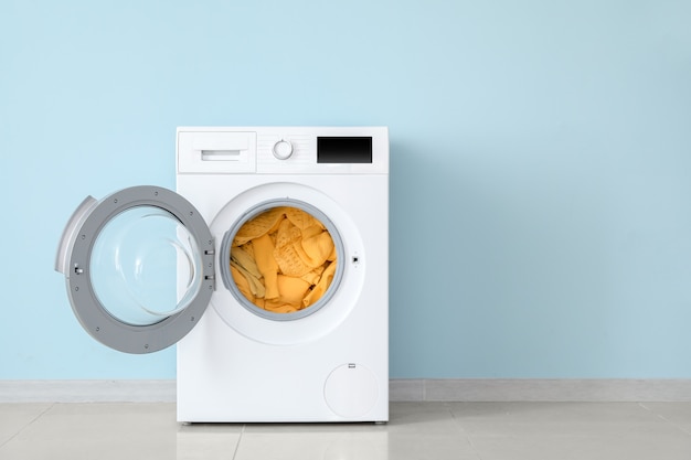 Modern washing machine with laundry near color wall