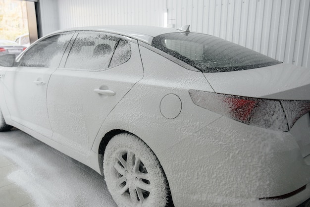 Modern washing with foam and high-pressure water of a white car. Car wash.