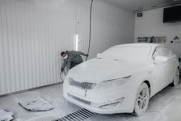 Современная стирка с пеной и водой под высоким давлением белого автомобиля. Автомойка.