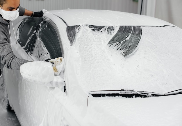 白い車の泡と高圧水による現代の洗浄。洗車。