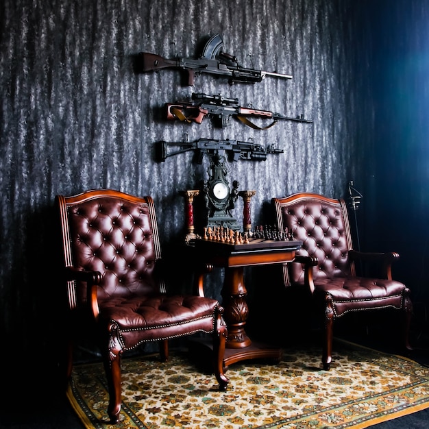 Modern weapons on wall in the interior of room with leather chairs and table for playing chess. Concept of collecting men toys. Copyright space for website or banner