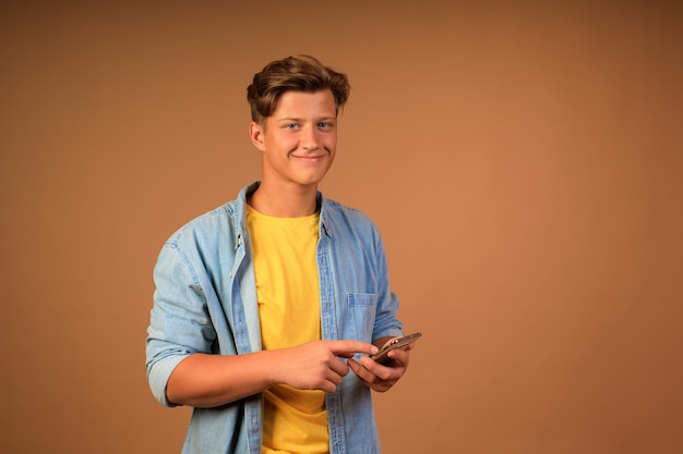 Modern werk op afstand. portret van een jonge man met een telefoon in zijn handen op een beige muur.