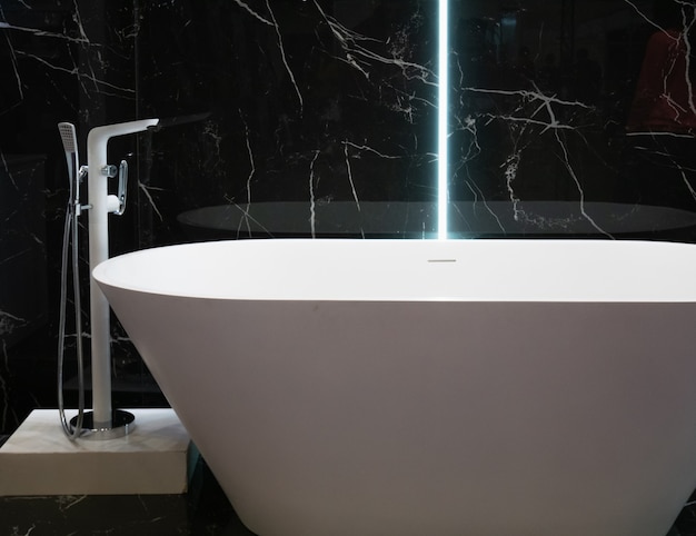 Modern white bathtub at hotel apartment with black marble wall interior design at bathroom