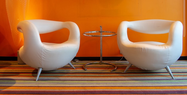 写真 オレンジ色の壁の部屋のカラフルなカーペットの上のモダンな白い椅子