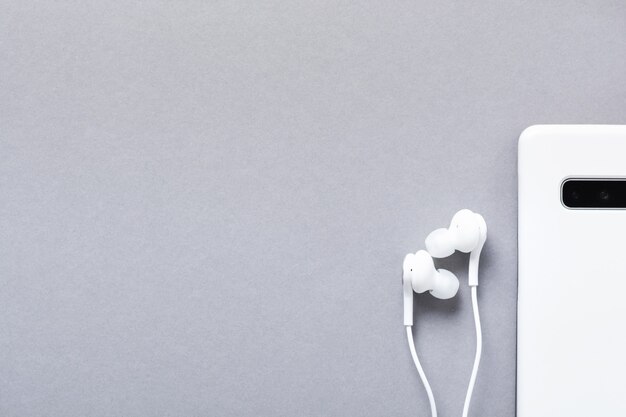 Modern White earphones and mobile phone on a gray