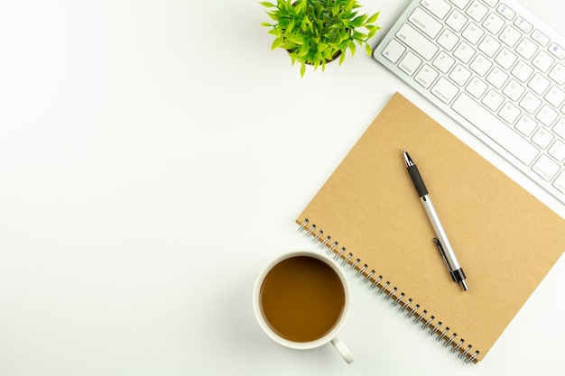 Modern white office desk with a computer keyboard, pen, notebook and cup of coffee. 