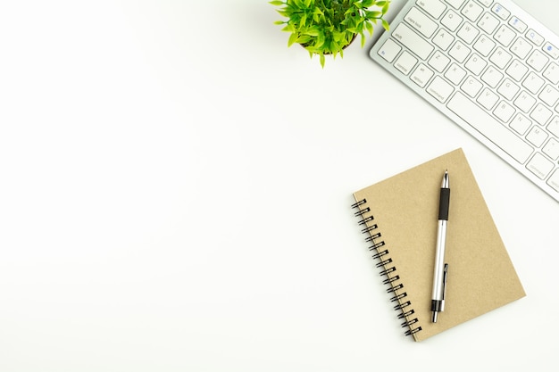 Modern white office desk with a computer keyboard, pen and a notebook. 