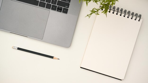 Modern white office desk with laptop computer pencil and empty spiral notepad for display your text